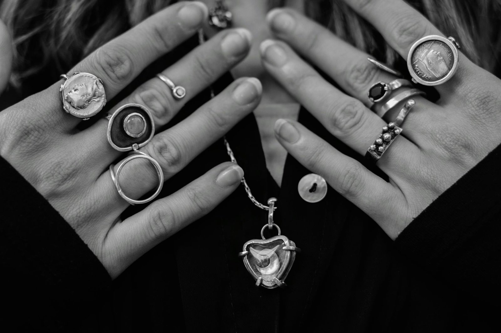 Close-up of hands adorned with various silver rings and necklace, showcasing fashion style.